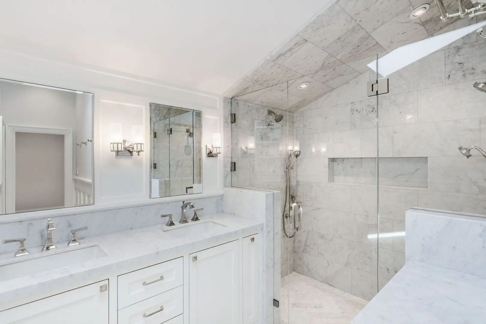 A bathroom with marble walls and floors, two sinks, and a large mirror.