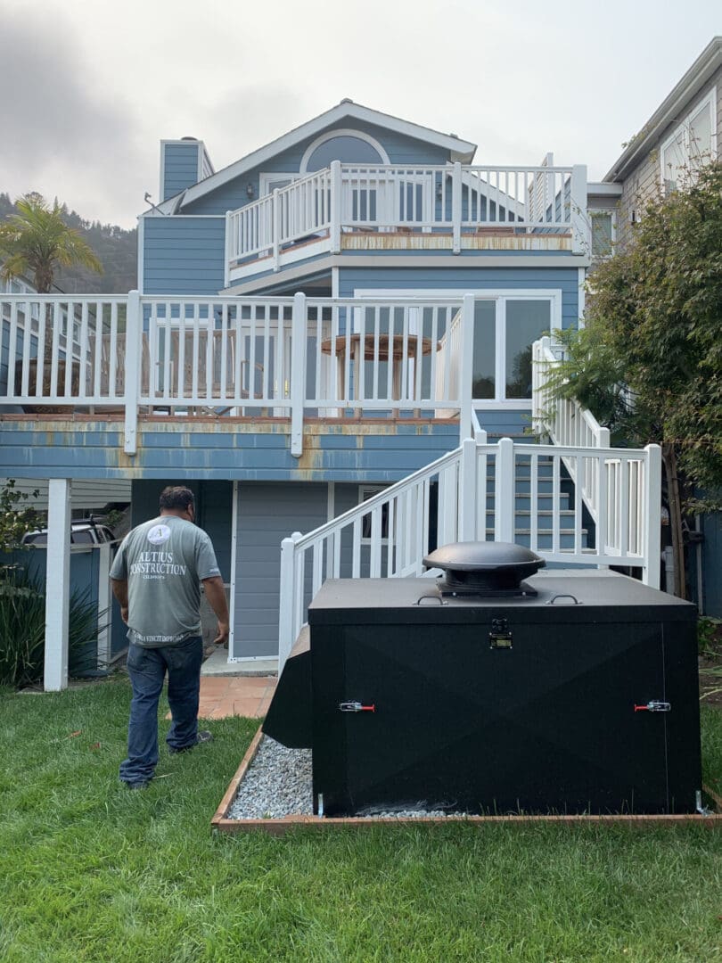 A man walking in front of a house with an outdoor grill.